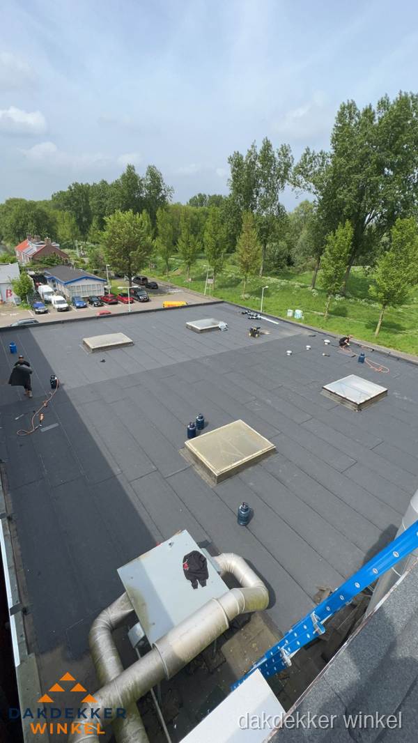 Dakdekker aan het werk op groot plat dak met bitumen in Winkel Dakdekker aan het werk op groot plat dak met bitumen in Winkel